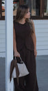 Woman in a brown outfit holding a white handbag against a building background