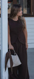 Woman in a brown outfit holding a white handbag against a building background