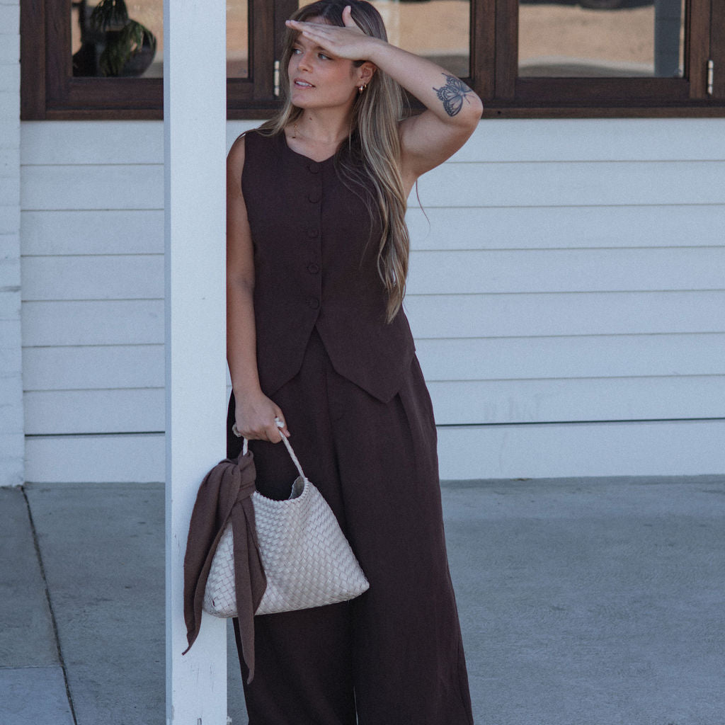 Woman in a brown dress standing outside a building with a white wall and glass door.