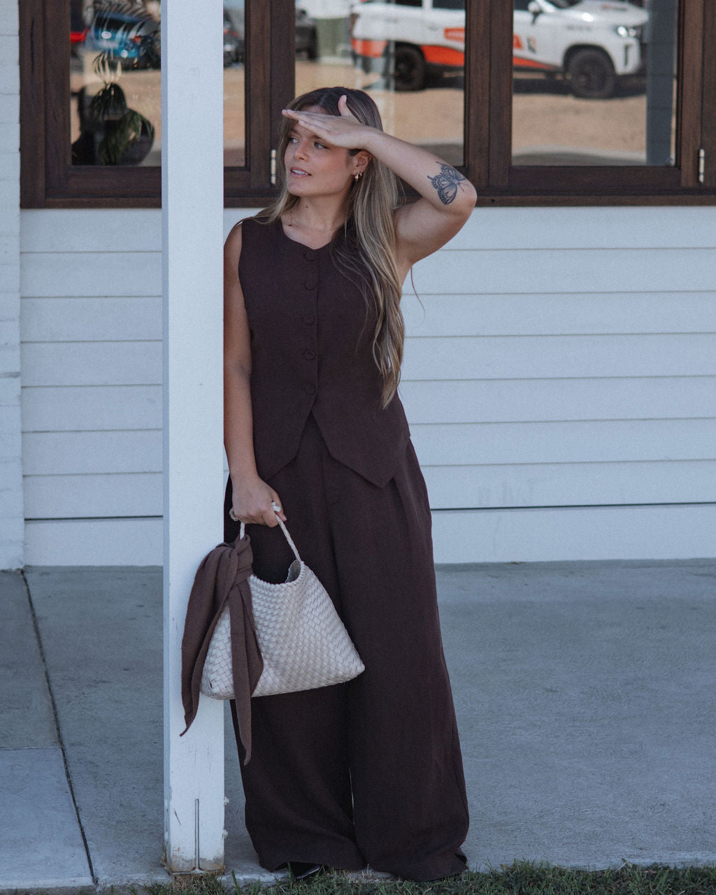 Woman in a brown dress standing outside a building with a white wall and glass door.