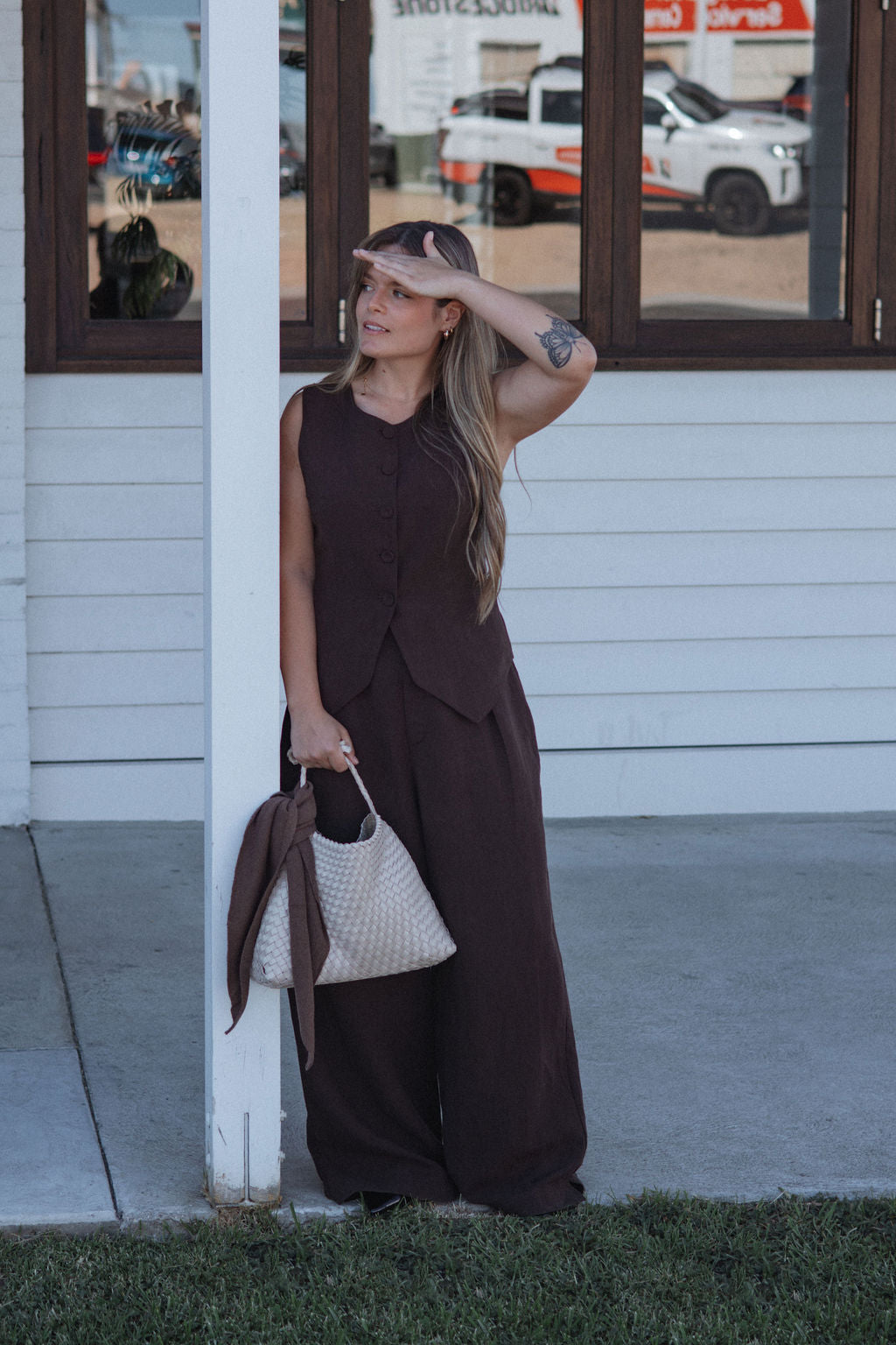 Woman in a brown dress standing outside a building with a white wall and glass door.
