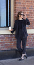 Woman in a black suit holding a coffee cup against a brick wall.