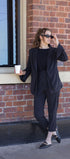 Woman in a black suit holding a coffee cup against a brick wall.