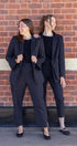 Two women in matching black suits standing against a brick wall.