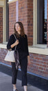 Woman holding a patterned scarf and a white handbag against a brick building background