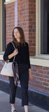 Woman holding a patterned scarf and a white handbag against a brick building background
