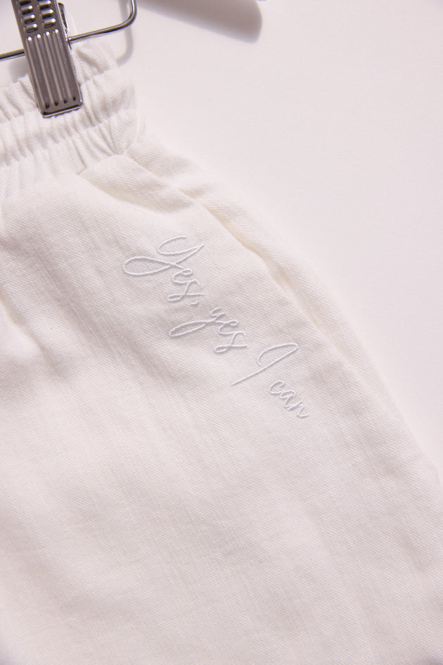 White garment with 'Justine' embroidered on it, hanging against a white background.