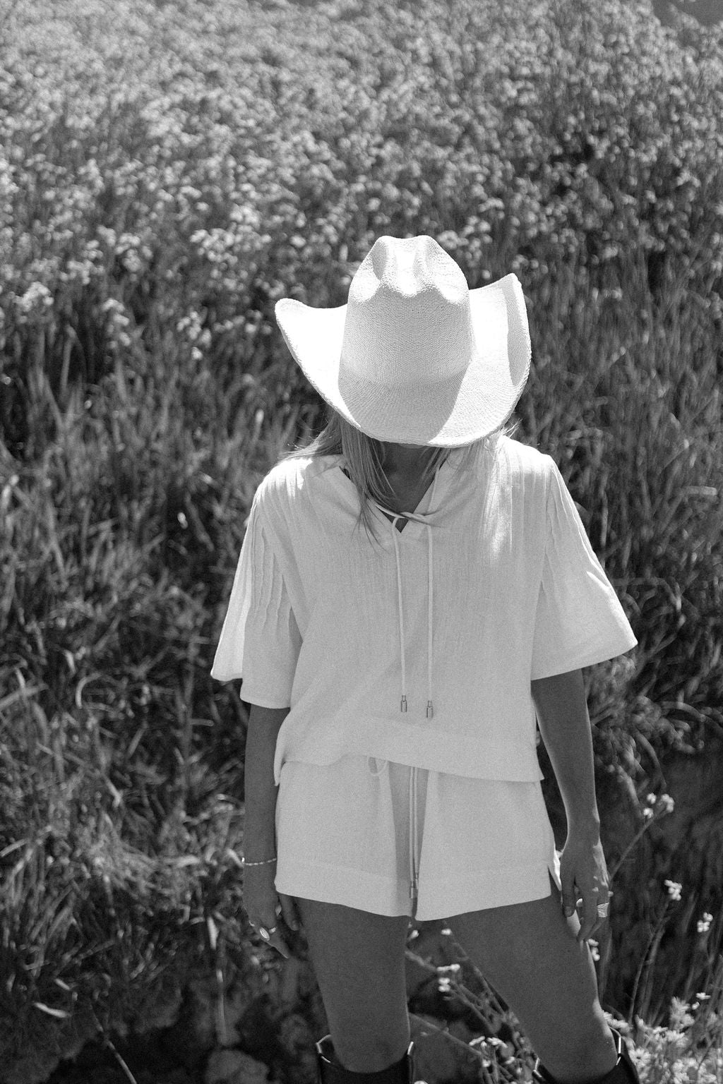 Person wearing a white cowboy hat and outfit standing in a field of tall grass.