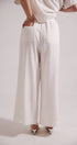 Person wearing white wide-leg pants and a white top on a light gray background