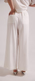 Person wearing white wide-leg pants and a white top on a light gray background