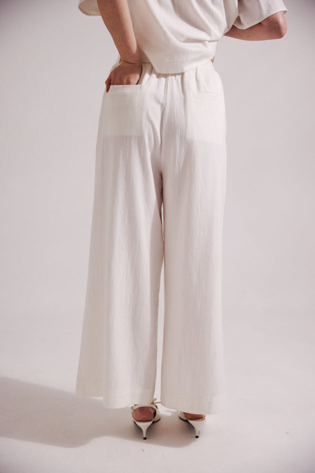 Person wearing white wide-leg pants and a white top on a light gray background