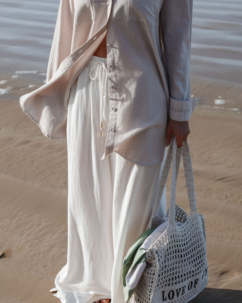 Person on a beach wearing a light outfit with a woven bag.