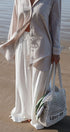 Person on a beach wearing a light outfit with a woven bag.
