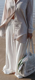 Person on a beach wearing a light outfit with a woven bag.