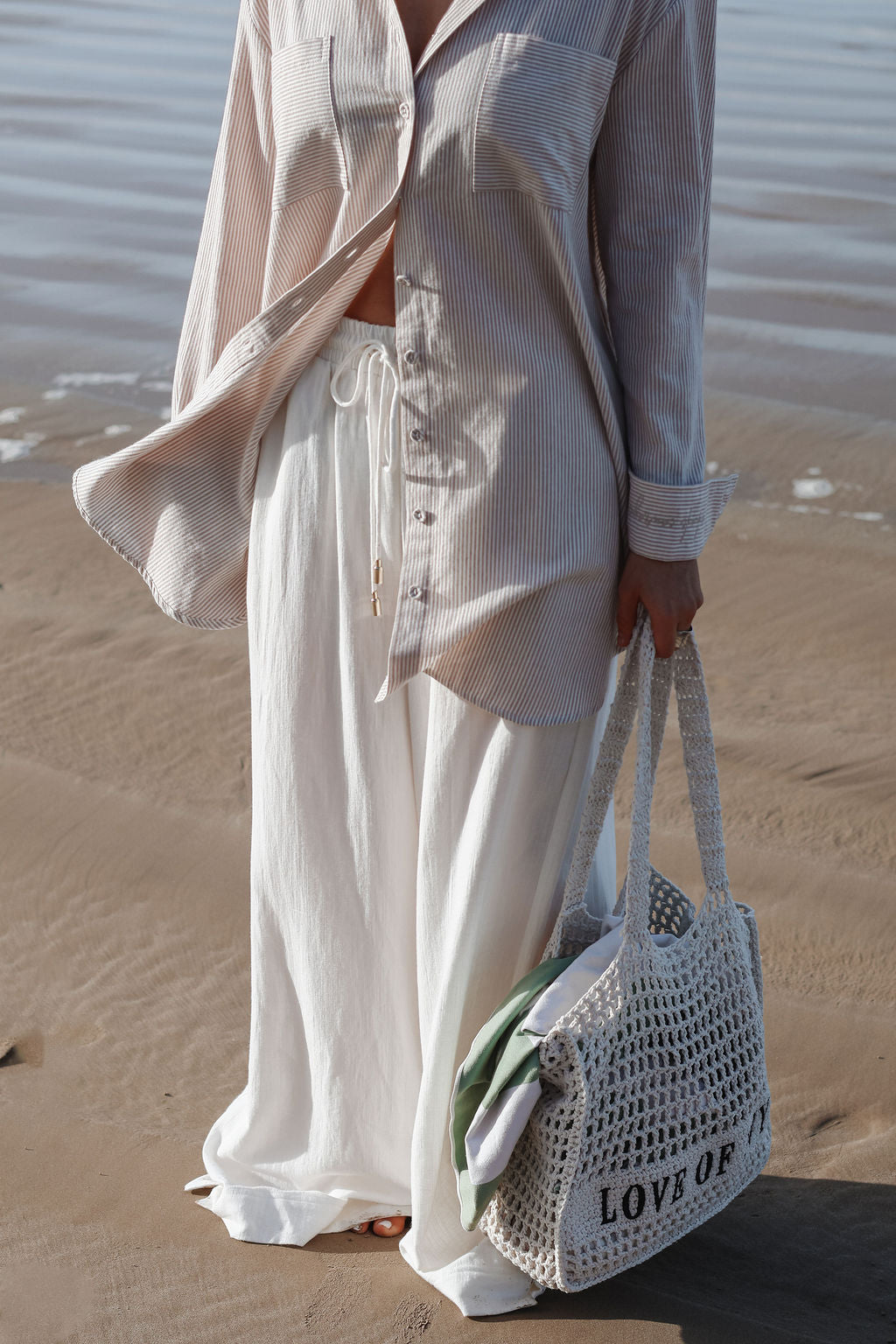 Person on a beach wearing a light outfit with a woven bag.
