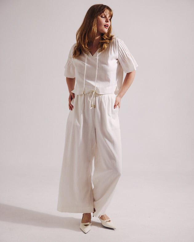 Woman wearing a white outfit with wide-leg pants on a plain background