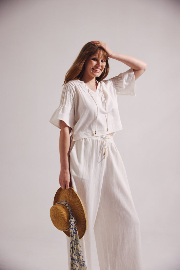 Woman in a white dress holding a straw hat against a plain background