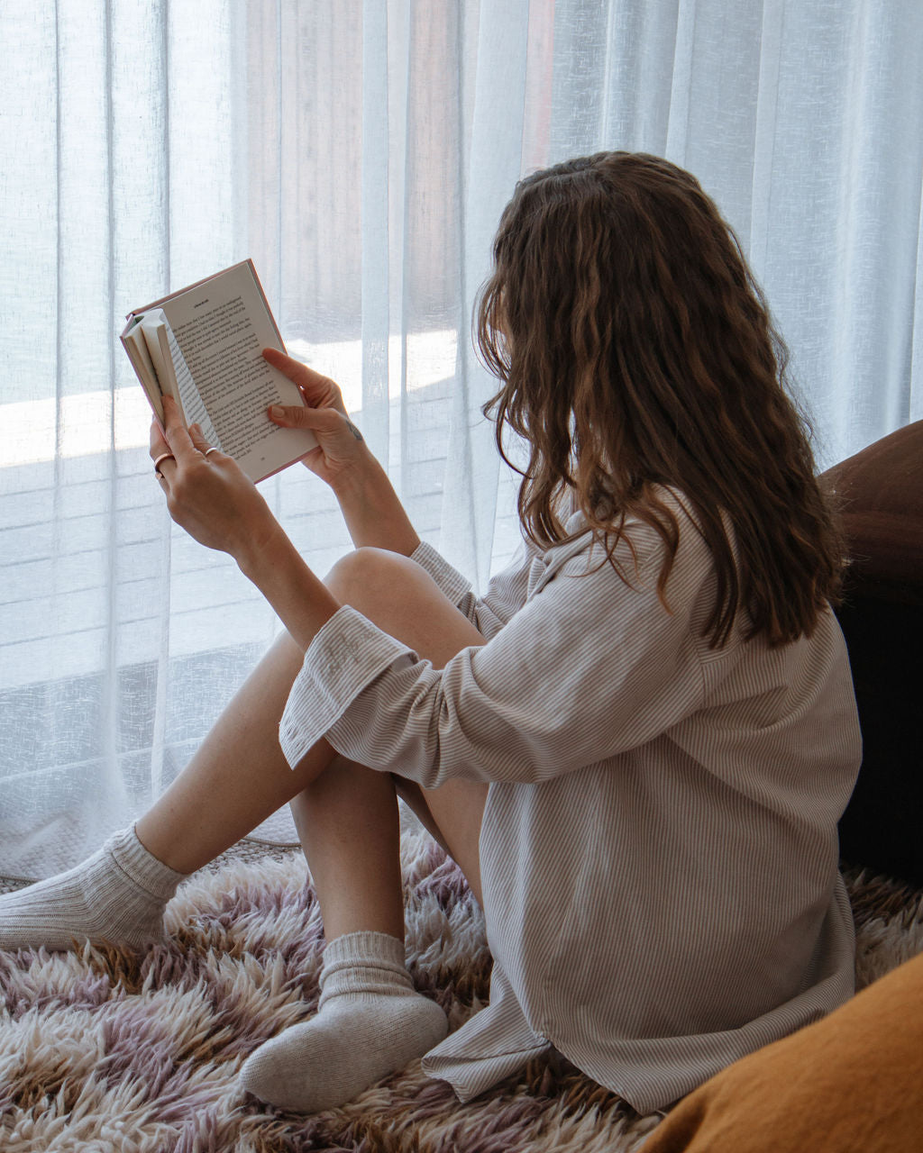 Person sitting on a couch reading a book in a softly lit room.