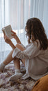Person sitting on a couch reading a book in a softly lit room.