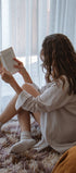 Person sitting on a couch reading a book in a softly lit room.