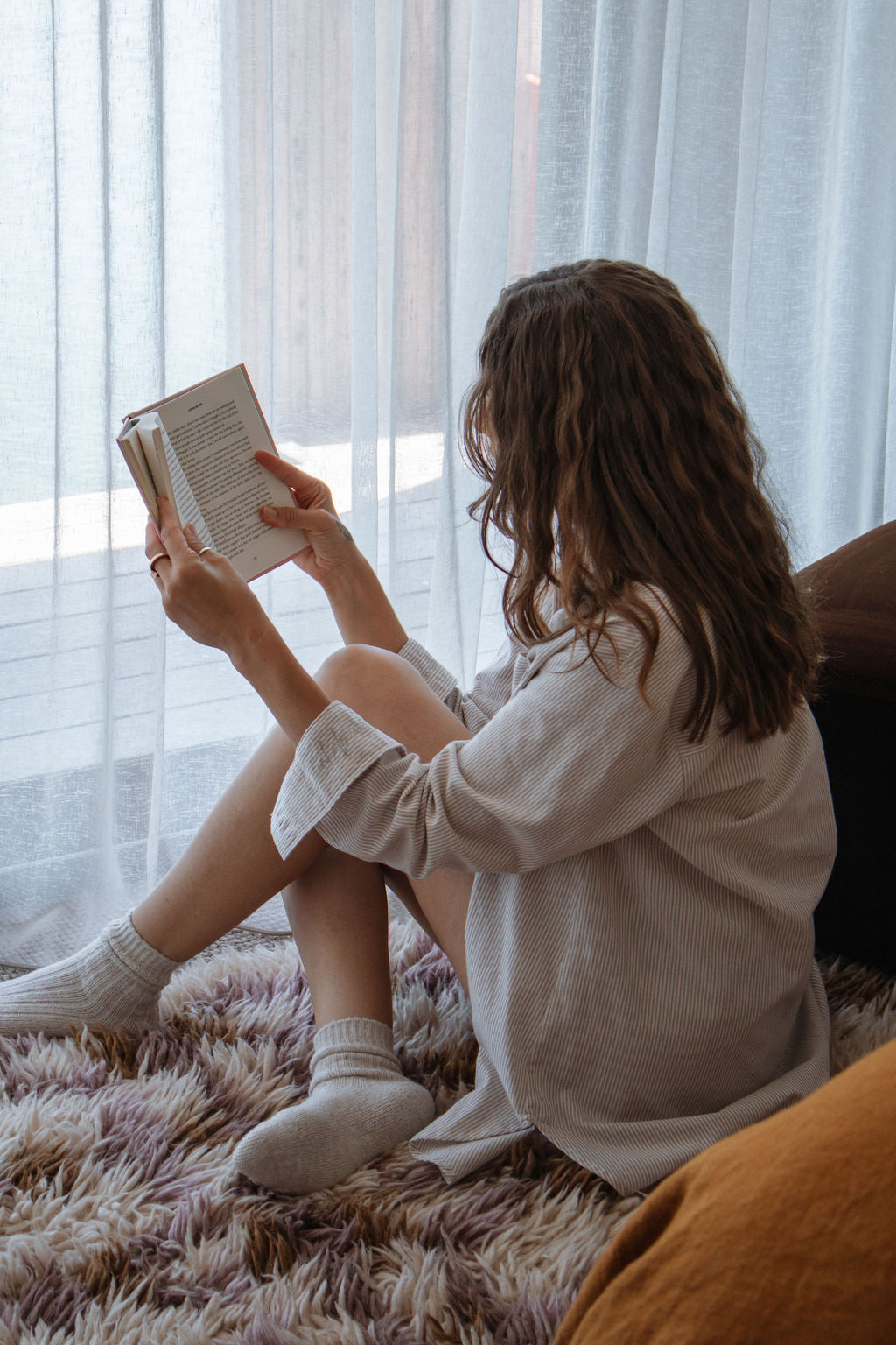 Person sitting on a couch reading a book in a softly lit room.