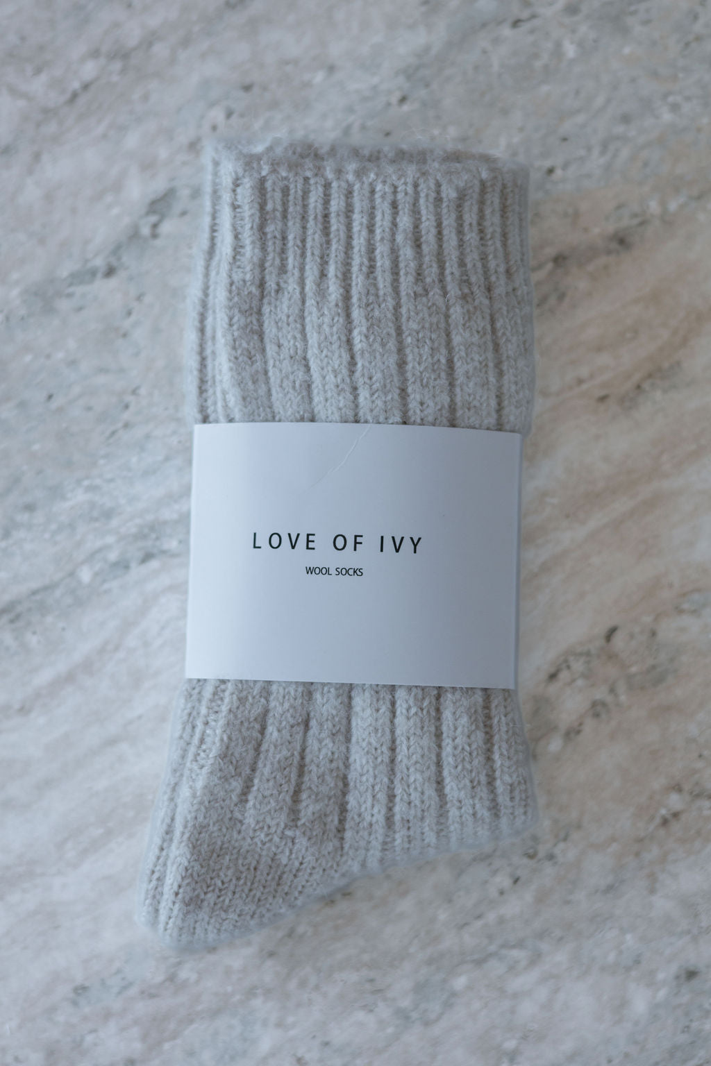 Packaged beige socks with 'LOVE OF IVY' label on a marble surface