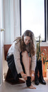 Woman sitting on a chair by a window, putting on black boots.