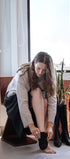 Woman sitting on a chair by a window, putting on black boots.