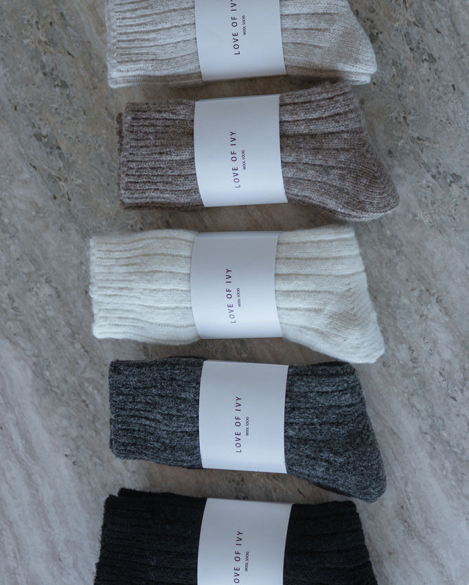 Five pairs of socks in black, gray, white, brown, and beige on a marble surface with 'Love of Ivy' labels.