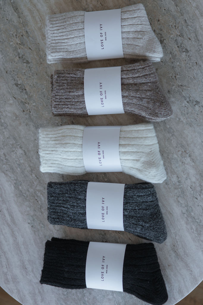 Five pairs of socks in black, gray, white, brown, and beige on a marble surface with 'Love of Ivy' labels.
