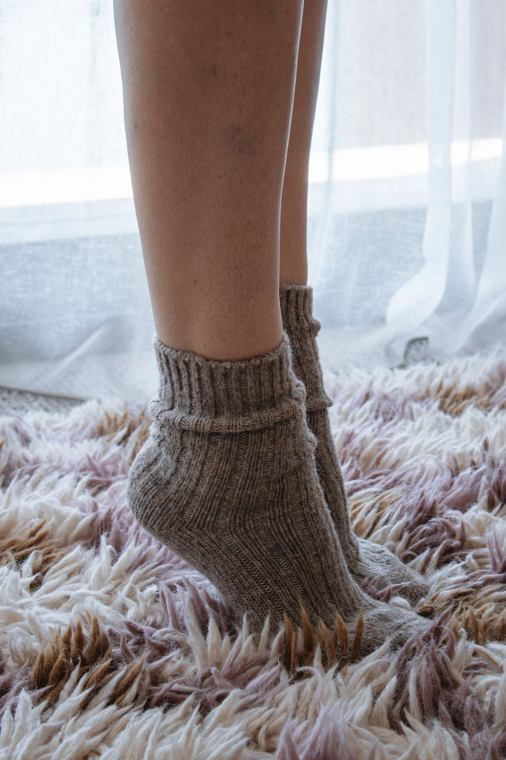 Person wearing brown knitted socks on a fluffy carpet