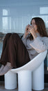 Woman sitting on a modern white chair by a large window, holding a mug.