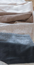 Close-up of folded triangle scarves in beige, brown, and light brown and black on a wooden surface.