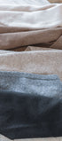 Close-up of folded triangle scarves in beige, brown, and light brown and black on a wooden surface.