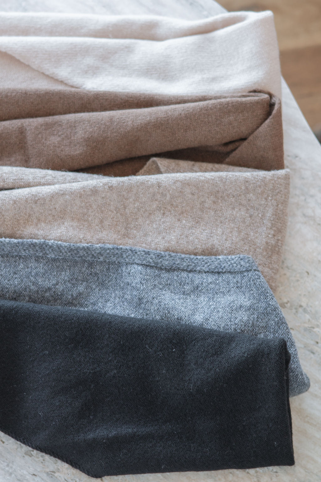 Close-up of folded triangle scarves in beige, brown, and light brown and black on a wooden surface.
