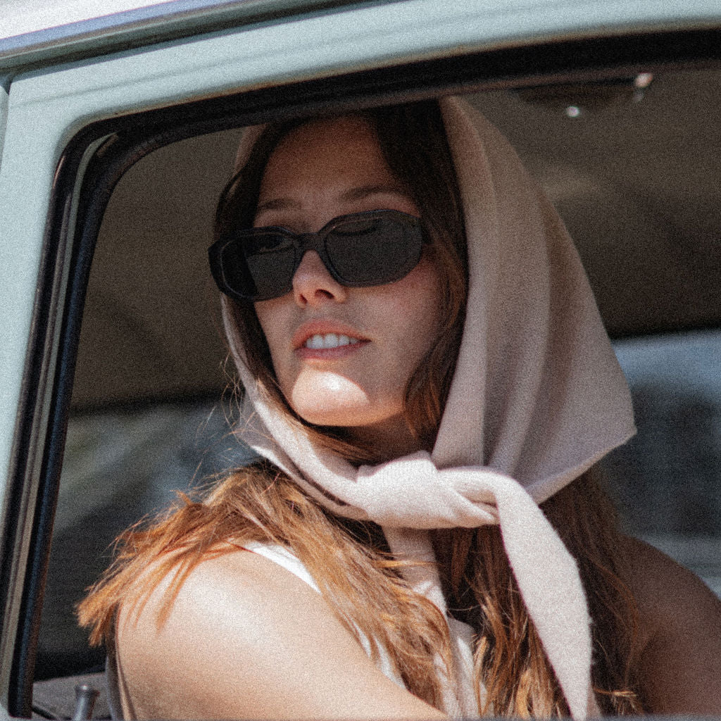 Woman wearing sunglasses and a headscarf, sitting inside a vehicle.