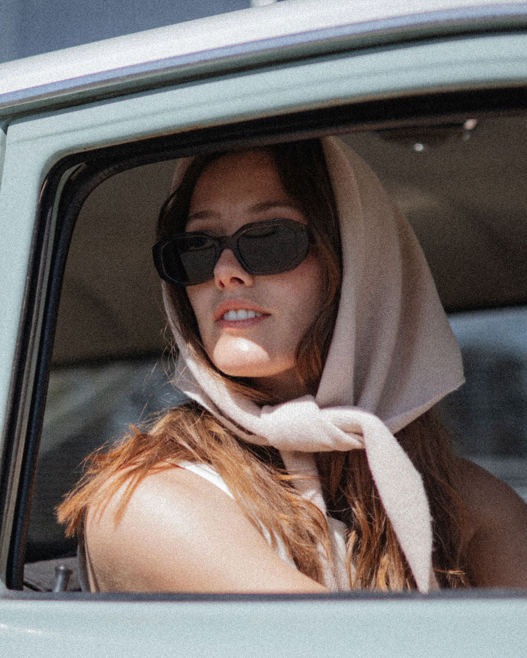Woman wearing sunglasses and a headscarf, sitting inside a vehicle.