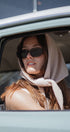 Woman wearing sunglasses and a headscarf, sitting inside a vehicle.