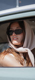Woman wearing sunglasses and a headscarf, sitting inside a vehicle.