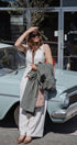 Woman standing in front of a vintage car holding a green jacket wearing a triangle scarf
