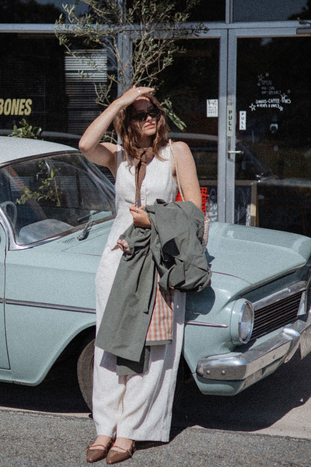 Woman standing in front of a vintage car holding a green jacket wearing a triangle scarf